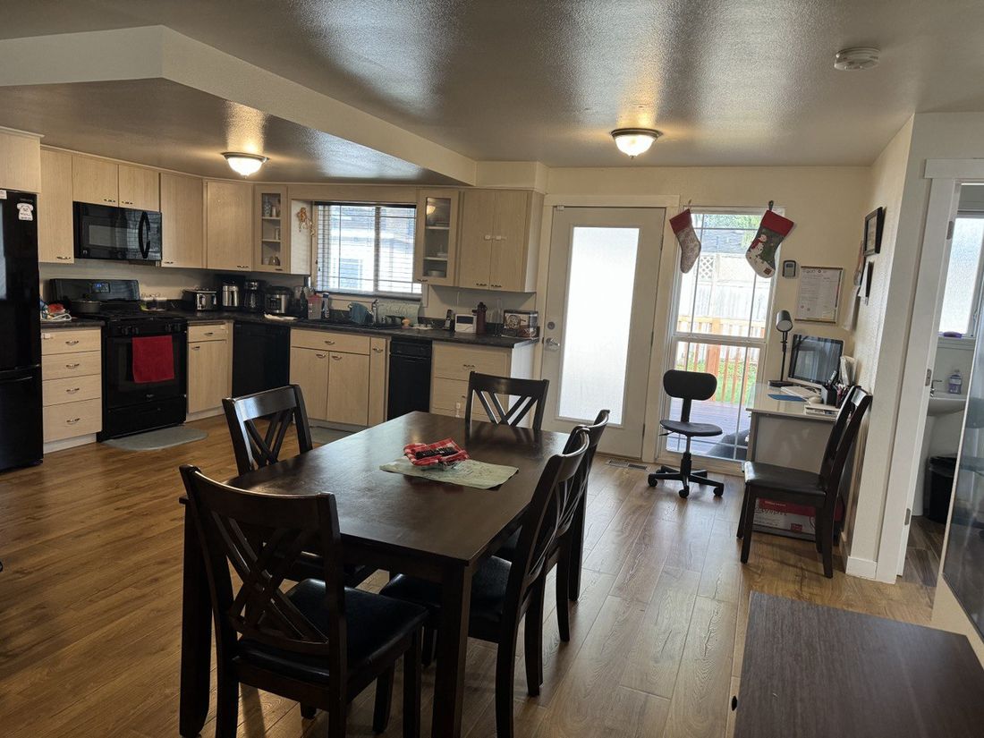 Open kitchen and dining area with warm wood floors, natural light, and a family dining table
